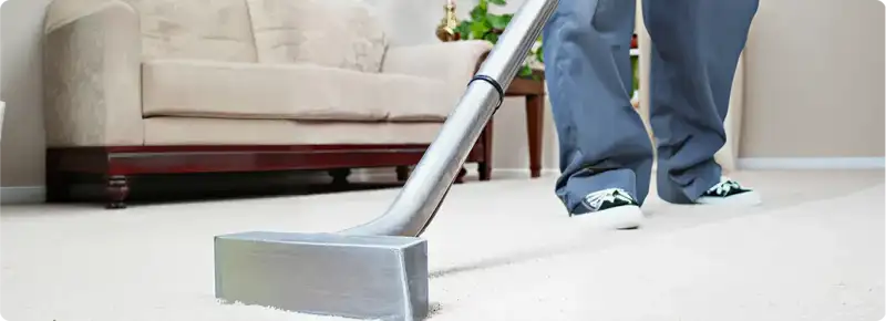 Carpet cleaning technician using a hot-water extraction wand on a light-colored carpet in a living room, Manchester, NH.