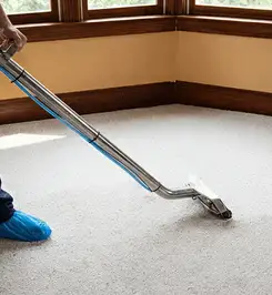 Steam carpet cleaning technician using a hot-water extraction wand on a residential carpet, wearing blue protective shoe covers Manchester, NH.