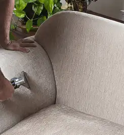 Professional upholstery cleaner deep-cleaning a fabric sofa with a handheld extraction tool and hose Manchester, NH.
