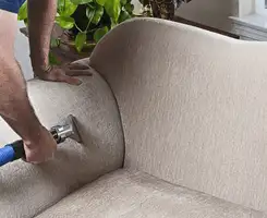 Professional upholstery cleaner deep-cleaning a fabric sofa with a handheld extraction tool and hose in Manchester, NH.
